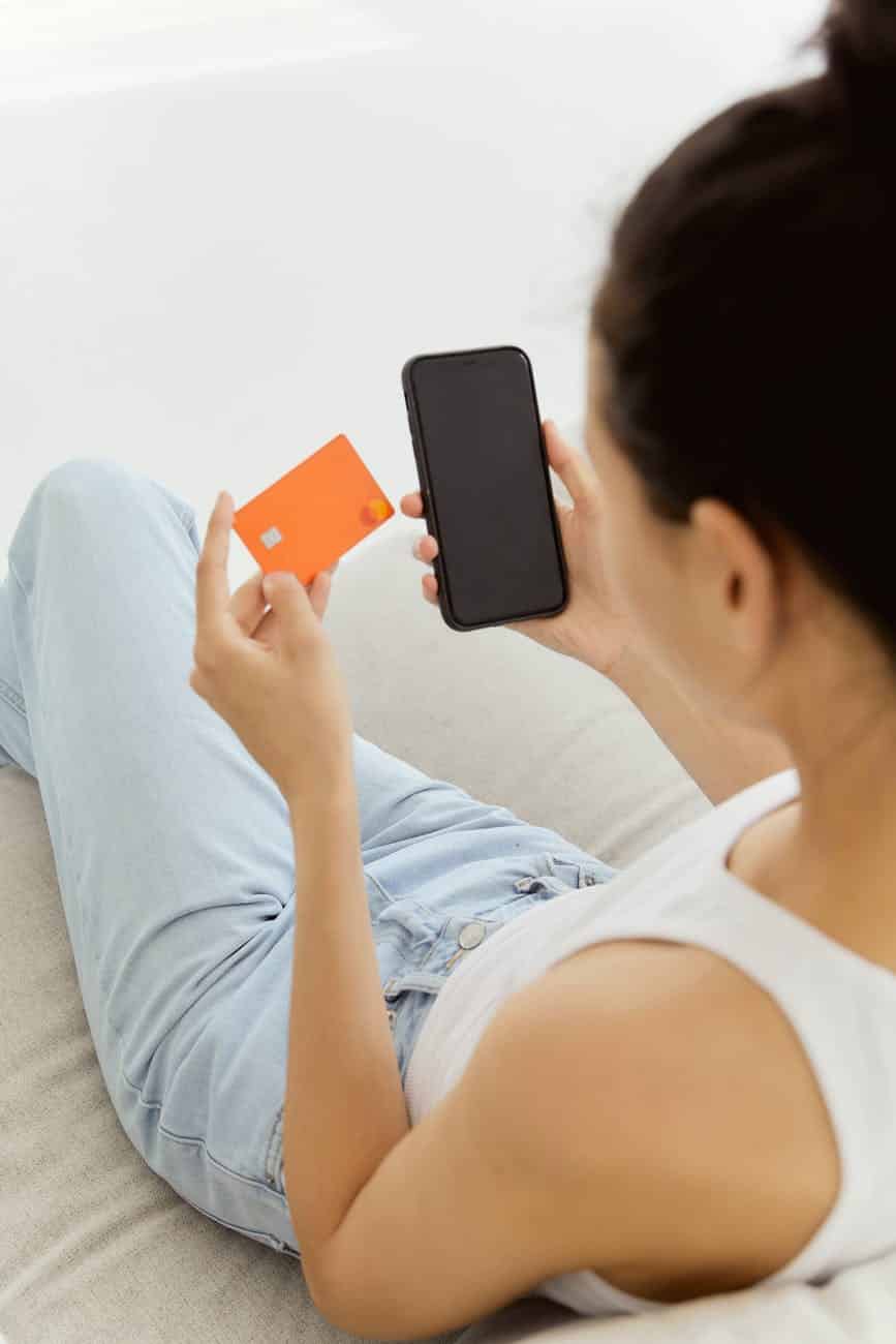 woman in white tank top holding smartphone and credit card